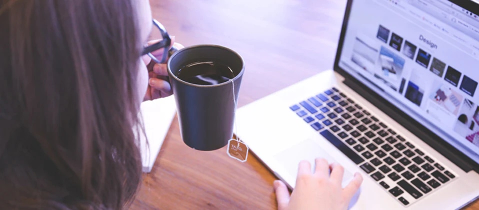 Person holding a tea mug while researching image editors on a laptop.