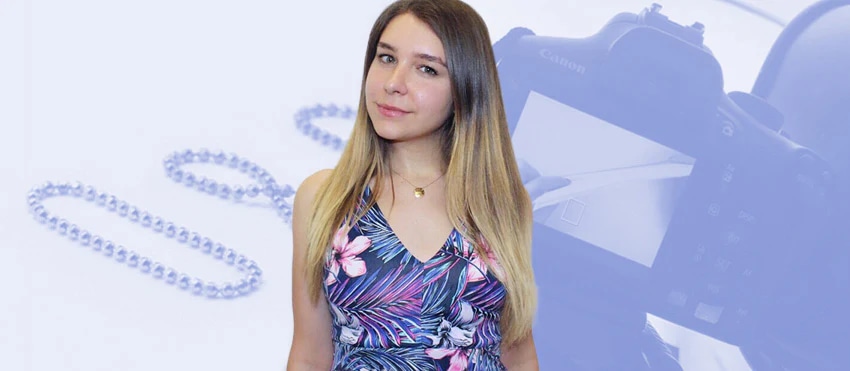 Woman in floral dress standing in front of blurred jewelry and camera background.