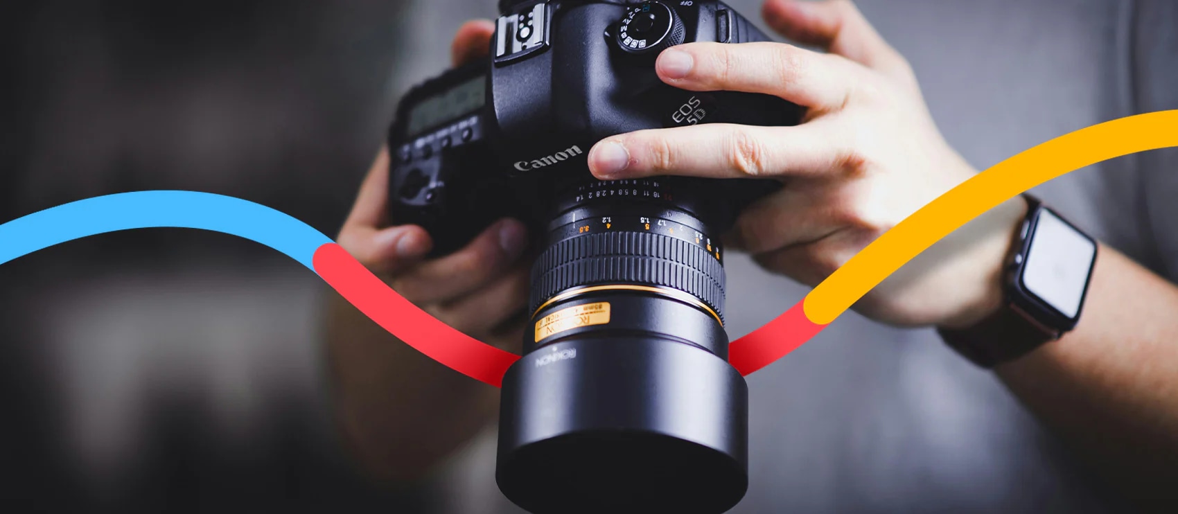 Close-up of a professional photographer holding a Canon DSLR camera with a colorful design element overlay on a blurred background.