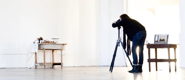 Photographer in a studio setting capturing product images with a tripod and camera, emphasizing a minimalistic background.